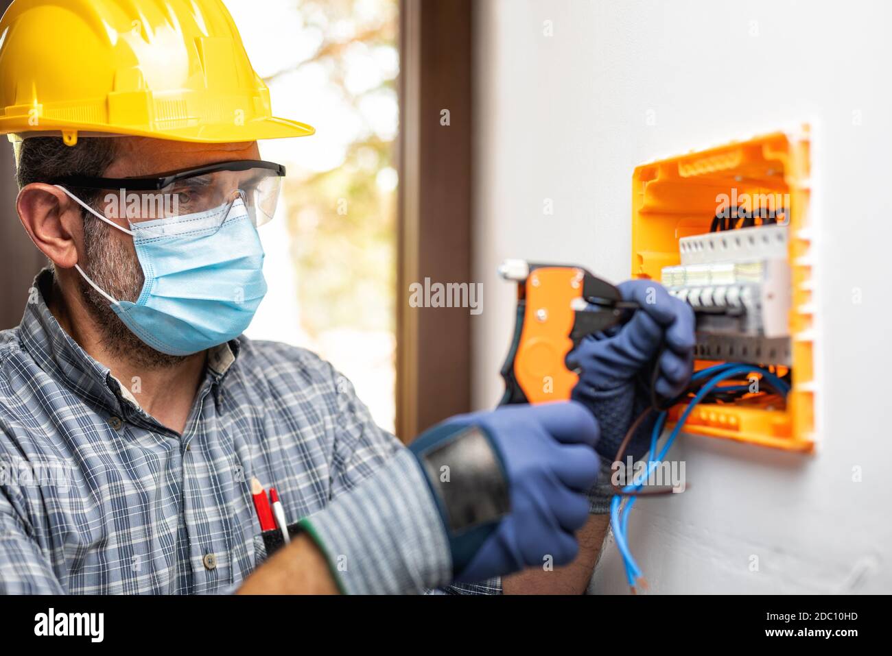 Electrician at work on an electrical panel protected by helmet, safety  goggles and gloves; wear the surgical mask to prevent the spread of  Coronavirus Stock Photo - Alamy