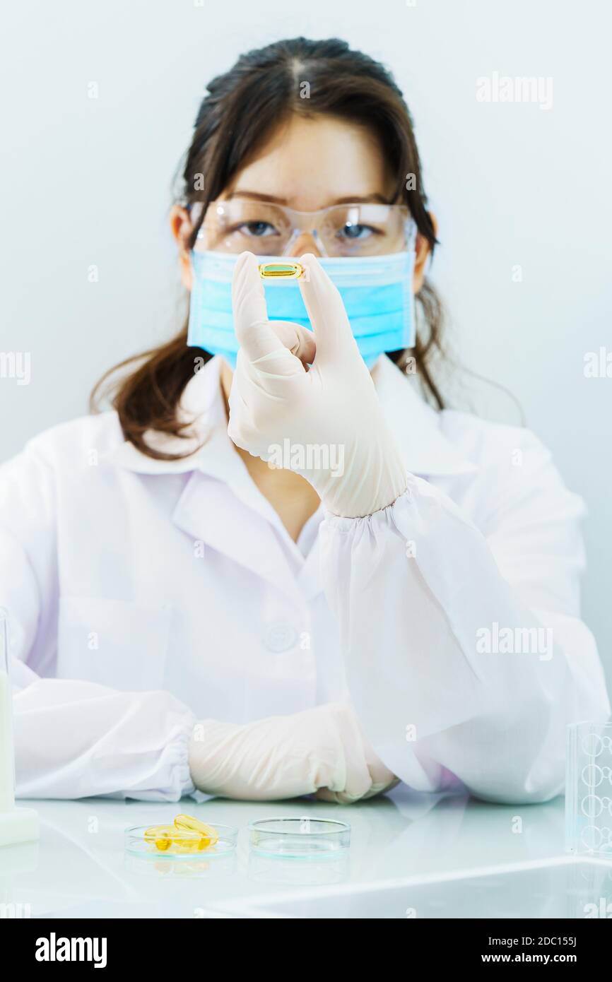 Close up Scientist hands putting in nitrile latex gloves holding Omega 3 capsule in labcoat doing experiments in lab Stock Photo
