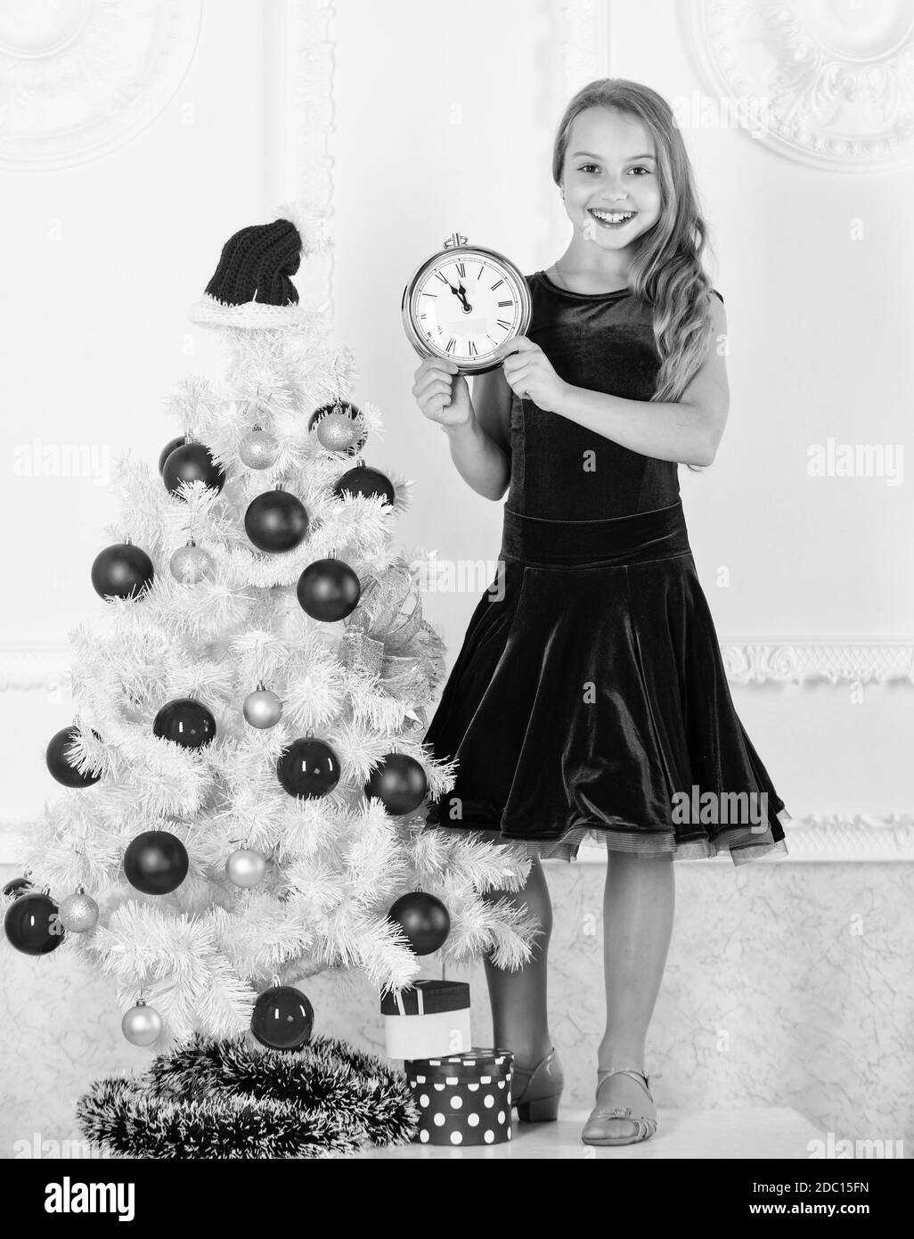 How much time left. Last minute till midnight. New year countdown. Last minute new years eve plans that are actually lot of fun. Girl kid santa hat costume with clock counting time to new year. Stock Photo