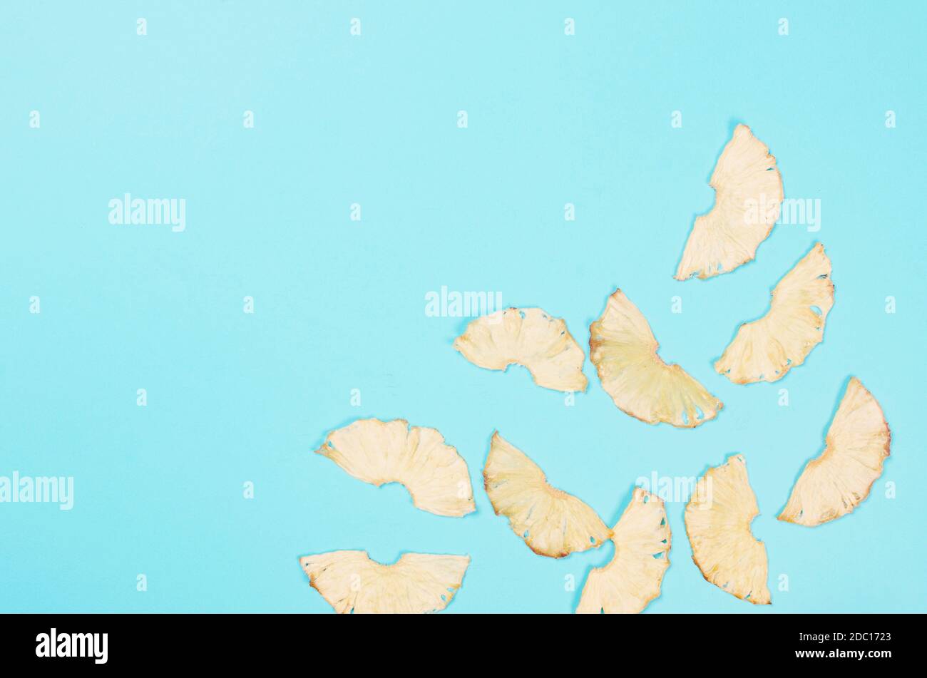 Dried pineapple wedges scattered on blue background. Fruit chips