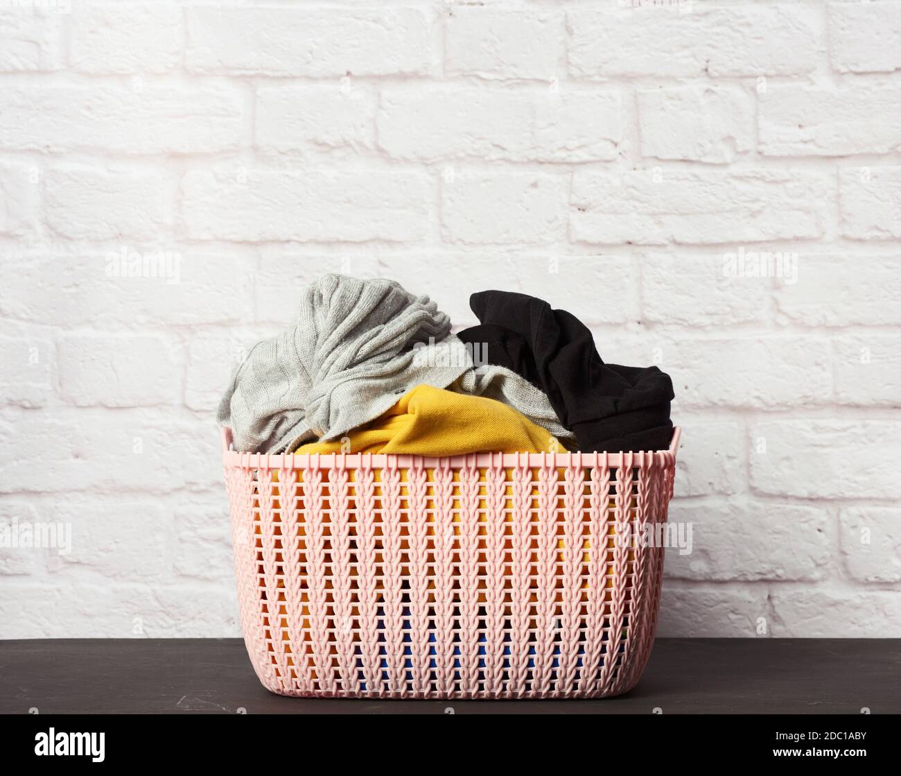 full pink plastic round laundry basket with white brick wall background