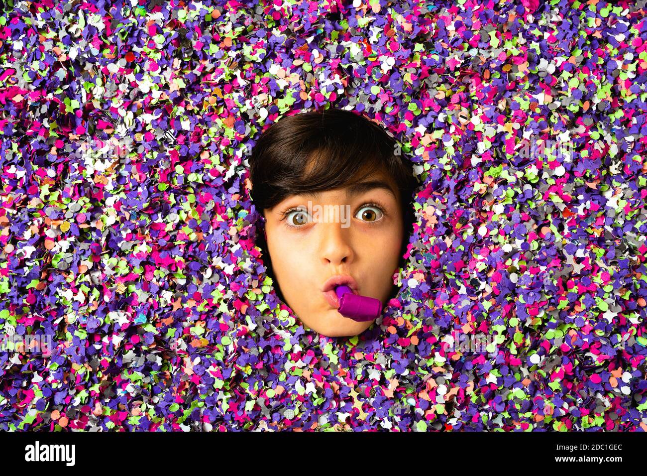 Surprised Young boy face blowing a party horn being surrounded by colored confetti Stock Photo