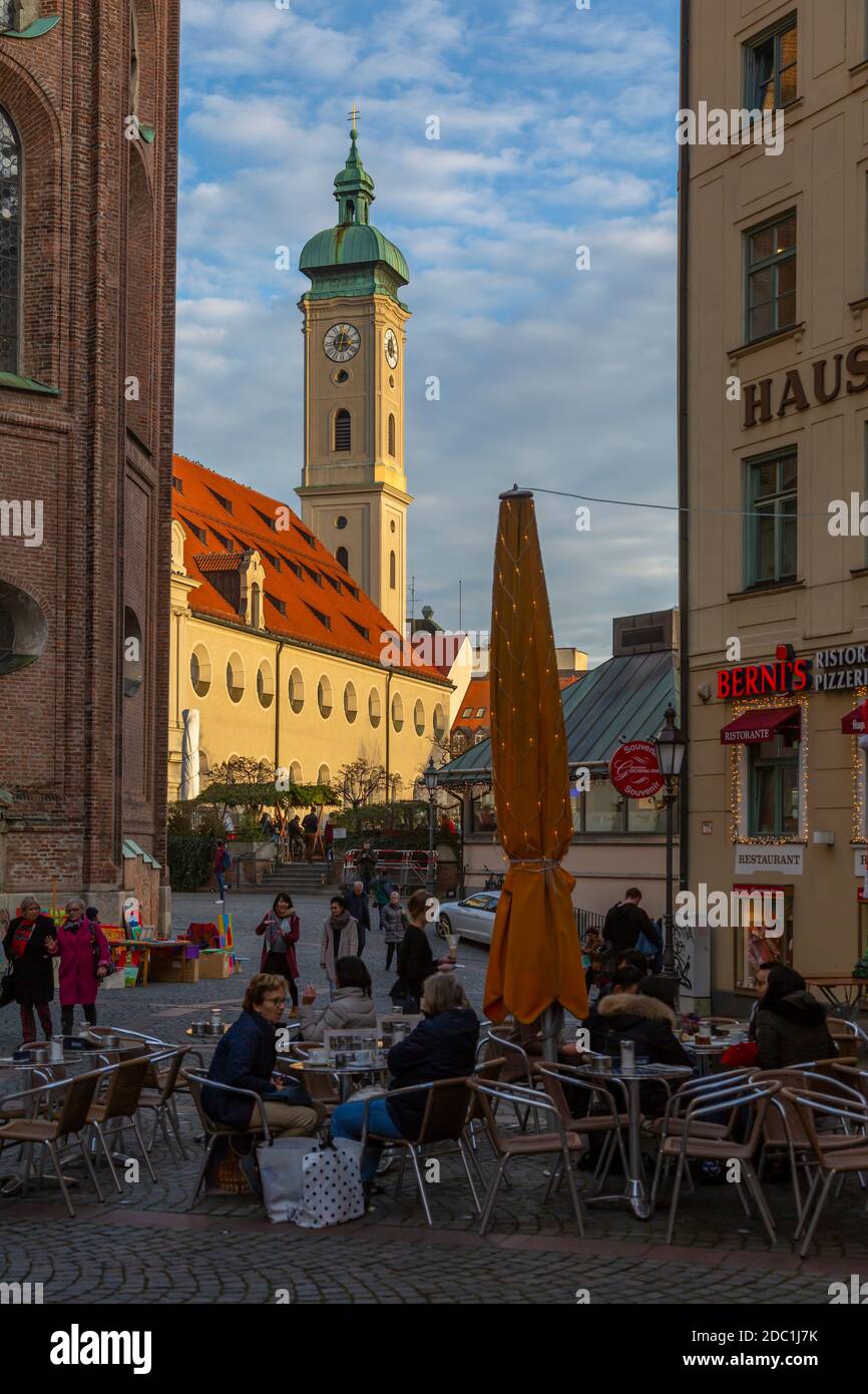 View of cafes and Heiliggeistkirche Church clock tower, Munich, Bavaria, Germany, Europe Stock Photo