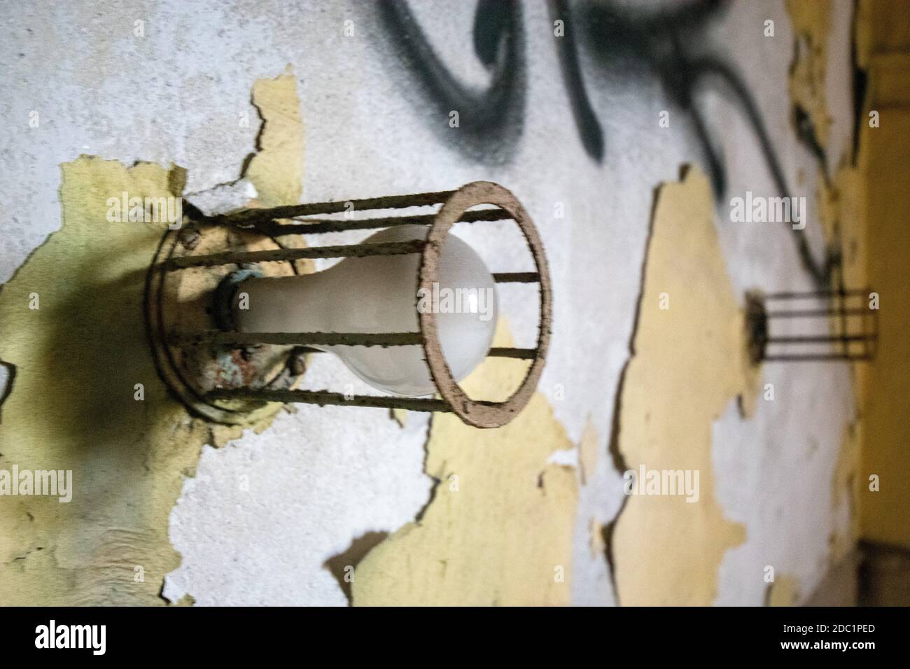 An Old Lightbulb Surrounded by Metal Bars on a Damaged Wall in an Abandoned Building Stock Photo