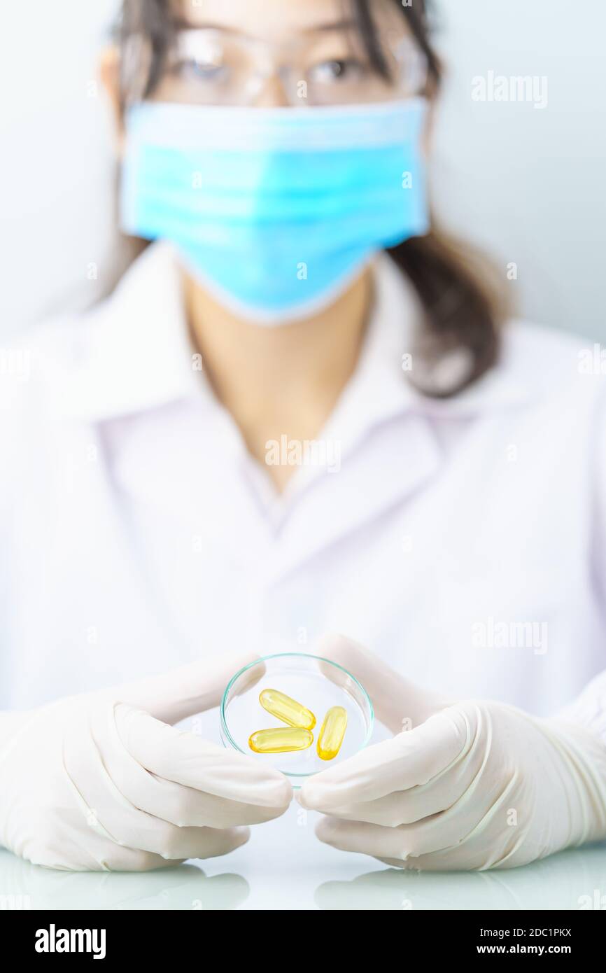 Close up Scientist hands putting in nitrile latex gloves holding Omega 3 capsule in labcoat doing experiments in lab Stock Photo