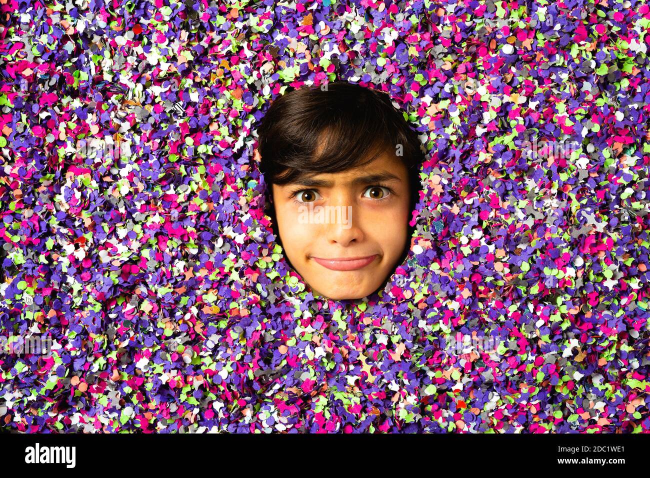 Young boy face making grimaces and being surrounded by colored confetti Stock Photo