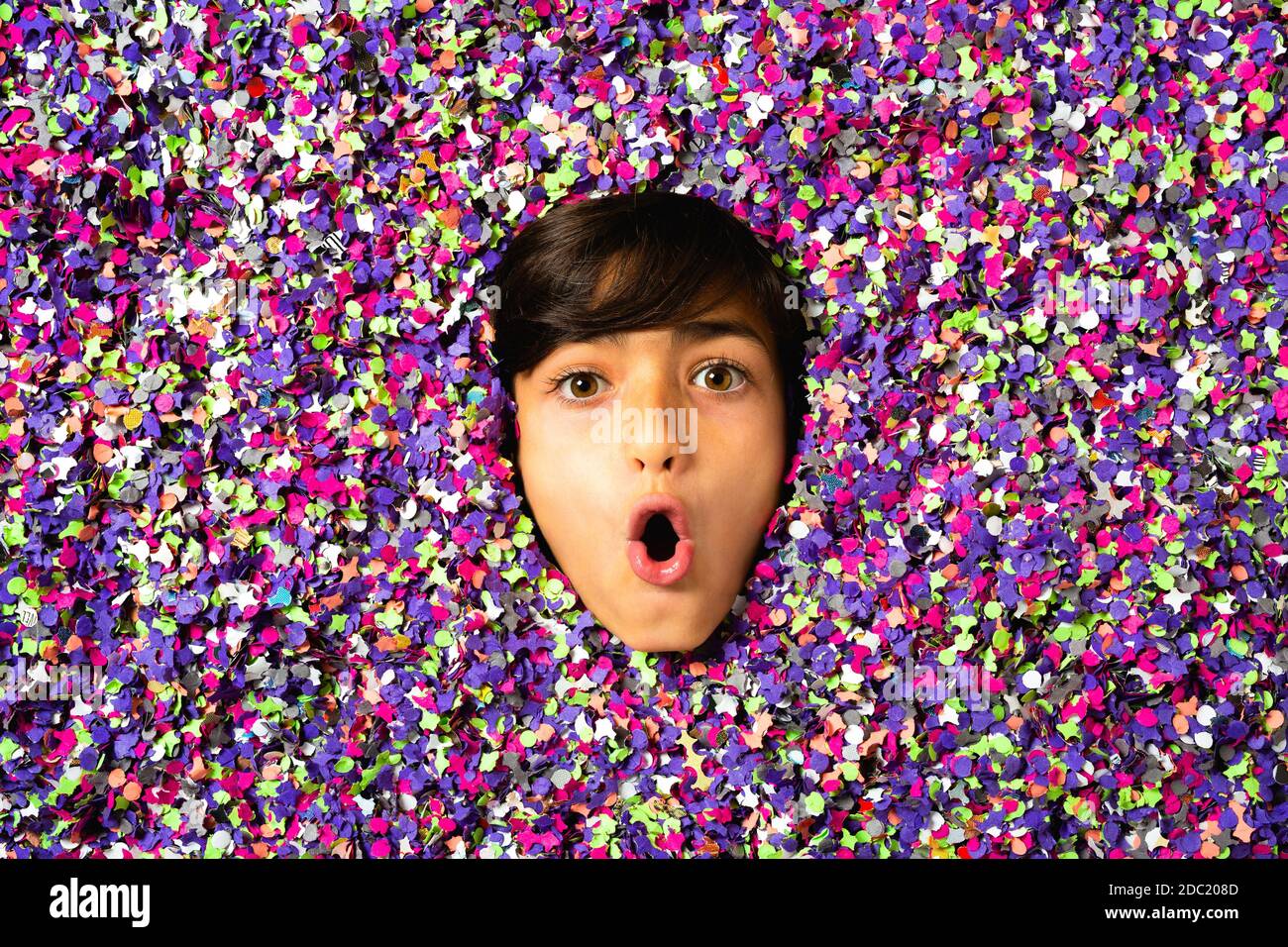 Surprised Young boy face being surrounded by colored confetti Stock Photo