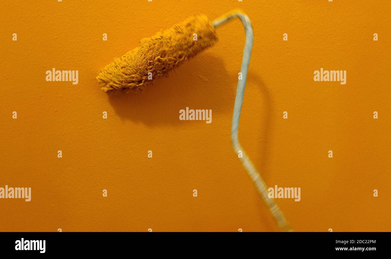 In motion paint roller against the orange wall Stock Photo