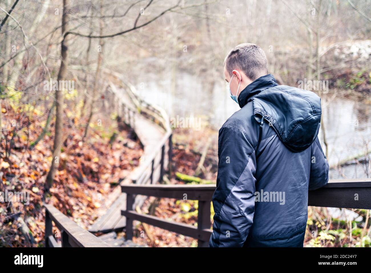 Man wearing a corona virus mask while walking outdoors in the nature in winter or autumn. Young person hiking the forest during coronavirus pandemic. Stock Photo