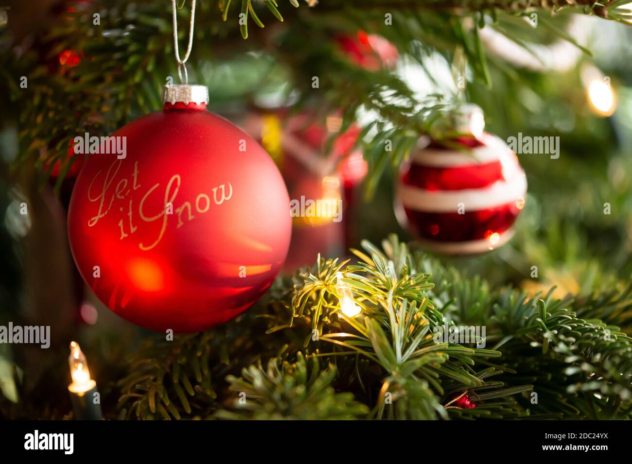 Decorated Christmas tree, real Nordmann fir in front of blurred background. Macro photography shows red Christmas baubles. English text is: let it sno Stock Photo