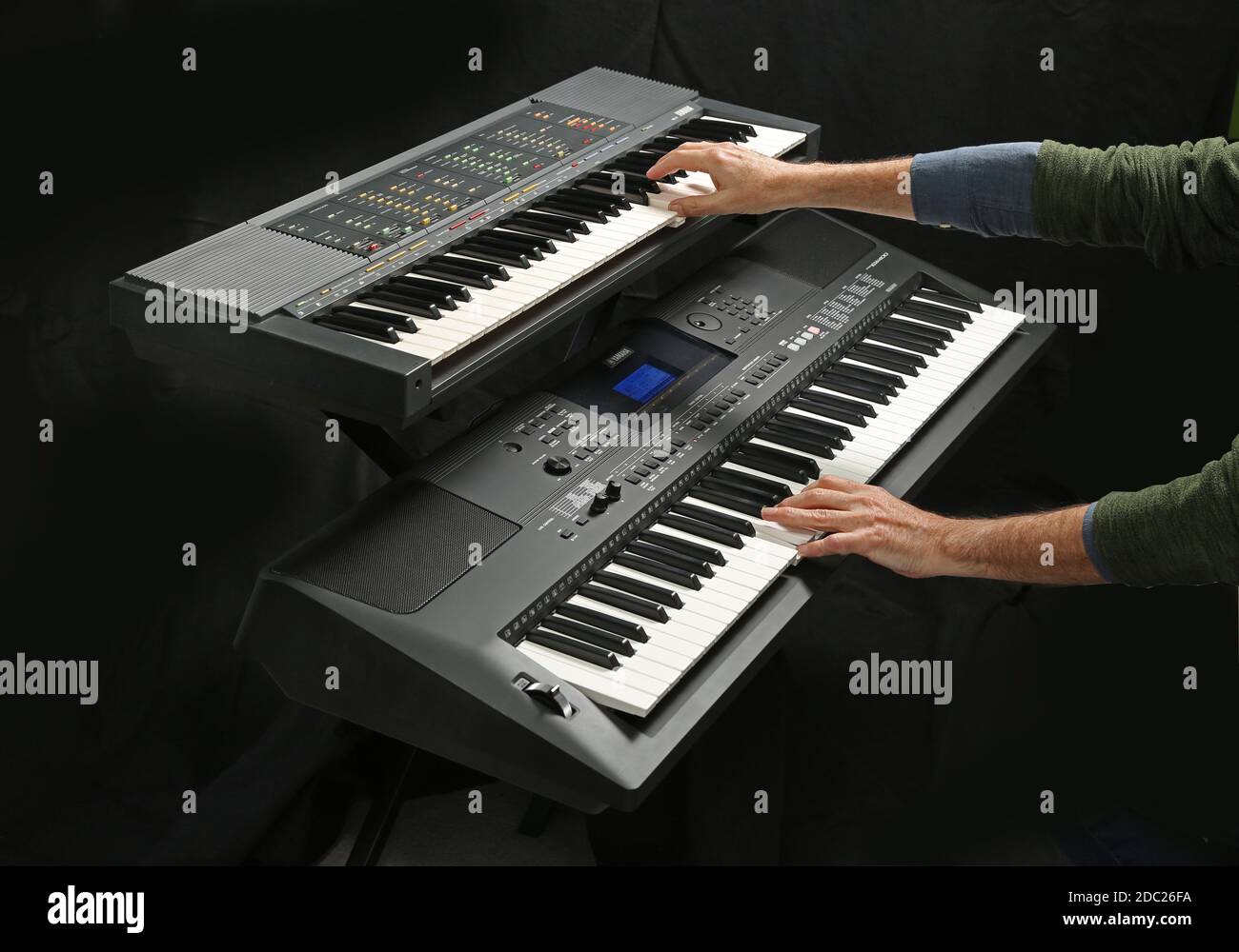 Studio shot of two Yamaha electronic keyboards being played; Models PSR 70 (top) and EW400. Shown on a folding, metal  X-frame stand. Stock Photo