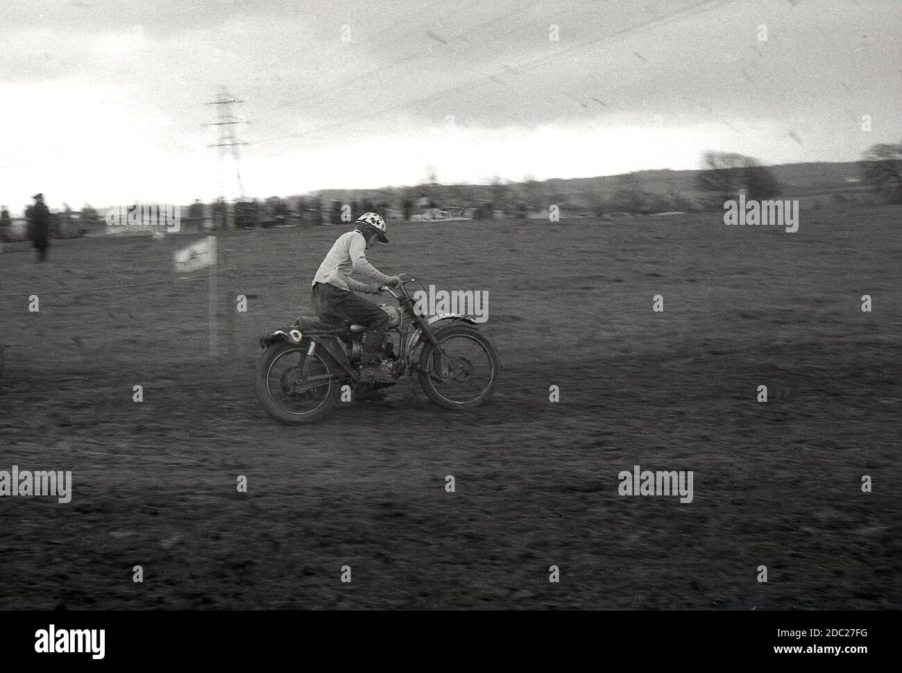 Late 1950s, a male competitor in a motorcycle scrambling event, riding across a muddy trail. Invented in 1924, in Camberley, Surrey, England, the bikes used to scramble in '50s and early '60s were little different from the road bikes of the time, with very little suspension. Today the sport is known as motocross – the French name for cross-country motorcycling – and referred to as Supercross in the USA. Stock Photo
