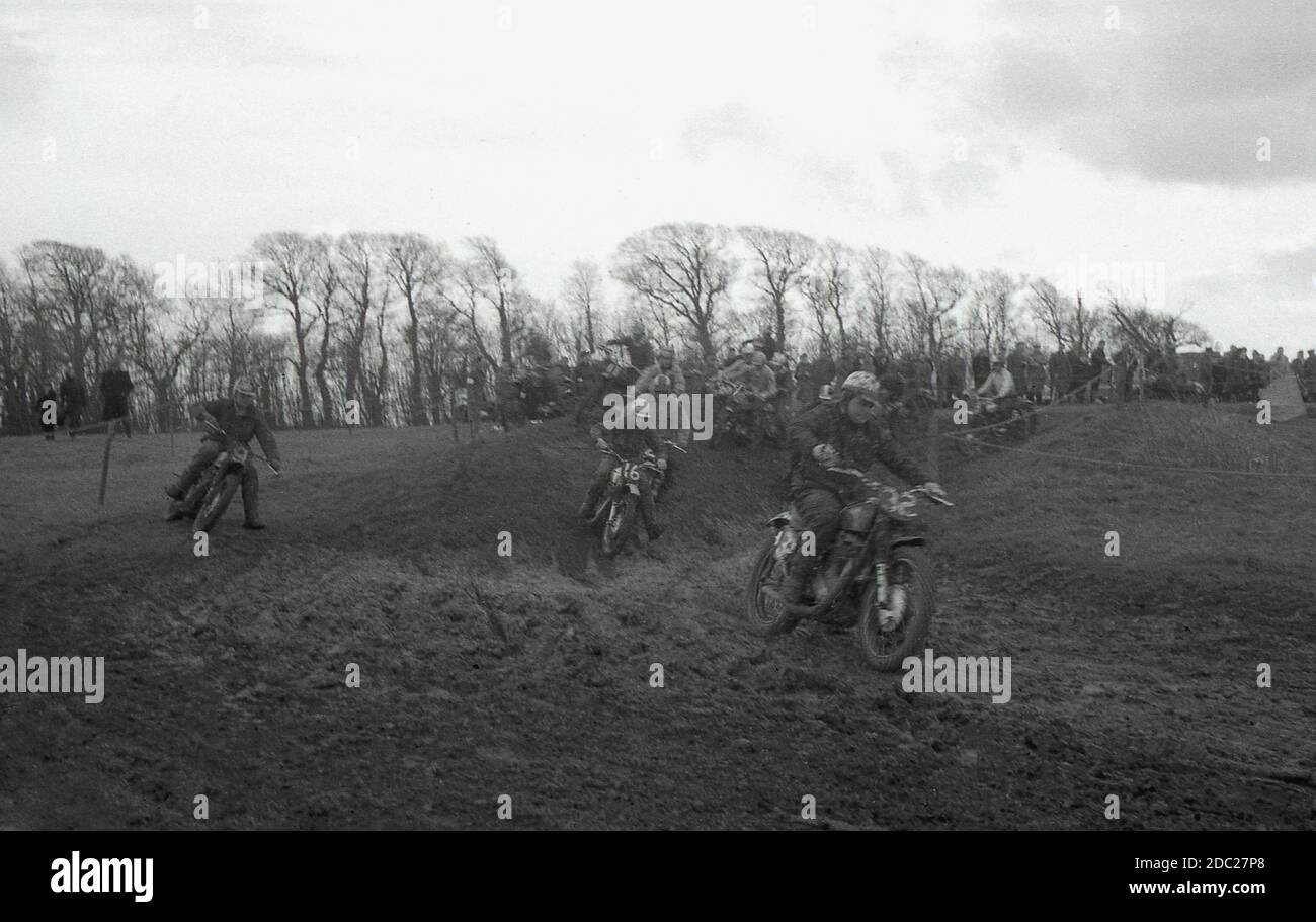 Late 1950s, male competitors taking part in a motorcycle scrambling event, riding across a muddy slope. Invented in 1924, in Camberley, Surrey, England, the bikes used to scramble in '50s and early '60s were little different from the road bikes of the time, with very little suspension. Today the sport is known as motocross – the French name for cross-country motorcycling – and referred to as Supercross in the USA. Stock Photo