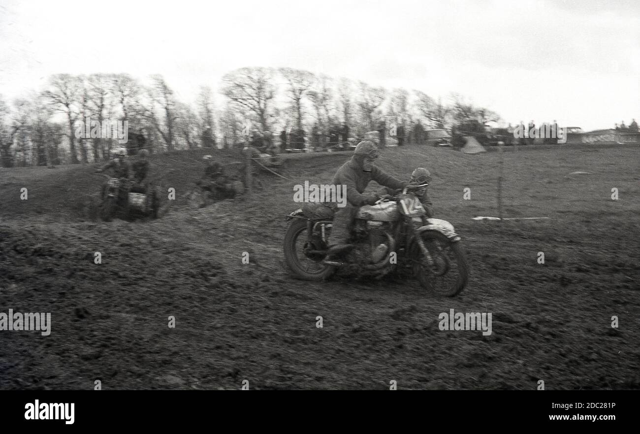 Late 1950s, male competitors taking part in a motorcycle scrambling event, riding across a muddy slope. Invented in 1924, in Camberley, Surrey, England, the bikes used to scramble in '50s and early '60s were little different from the road bikes of the time, with very little suspension. Today the sport is known as motocross – the French name for cross-country motorcycling – and referred to as Supercross in the USA. Stock Photo
