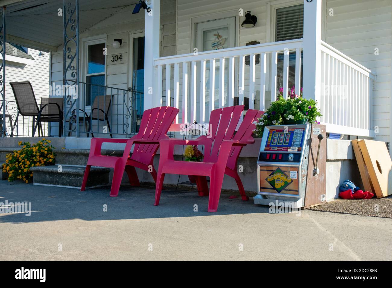 The Front of a Beach House With Two Red Lawn Chairs and a Slot Machine Next to Them Stock Photo