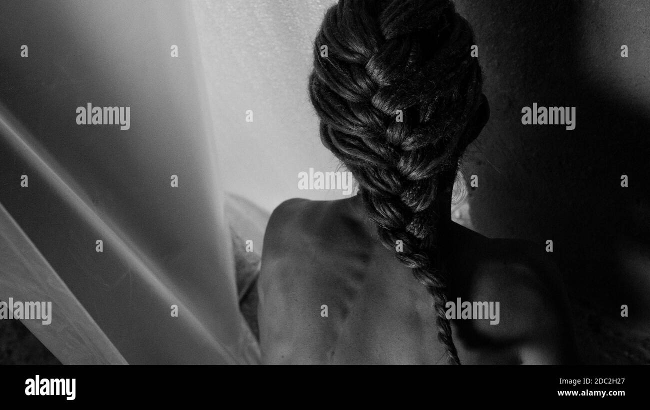The girl stands with her back to the camera, her hair is braided. Bw art photo. Stock Photo