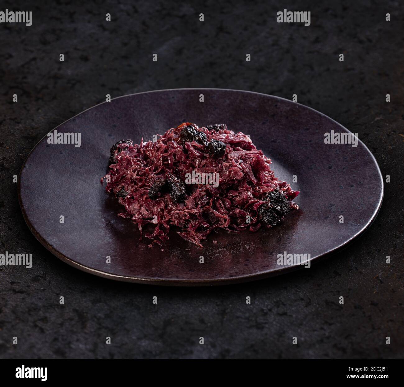 Braised red cabbage with dried prunes on black plate, black background Stock Photo