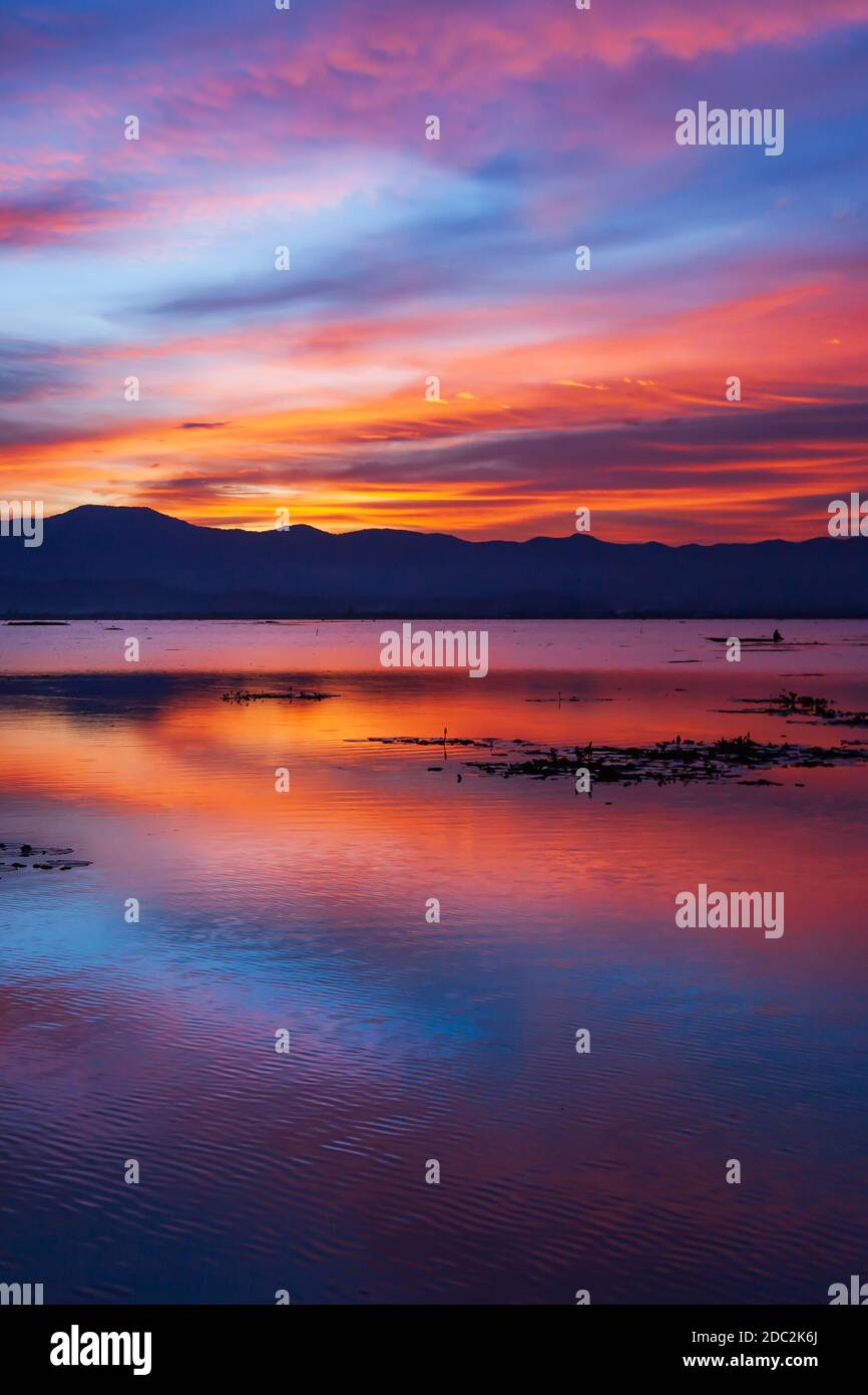 Dramatic clouds and sunset sky over the lake and mountains in backgrounds, colourful clouds and sky reflects on surface of the lake. Phayao, Thailand. Stock Photo