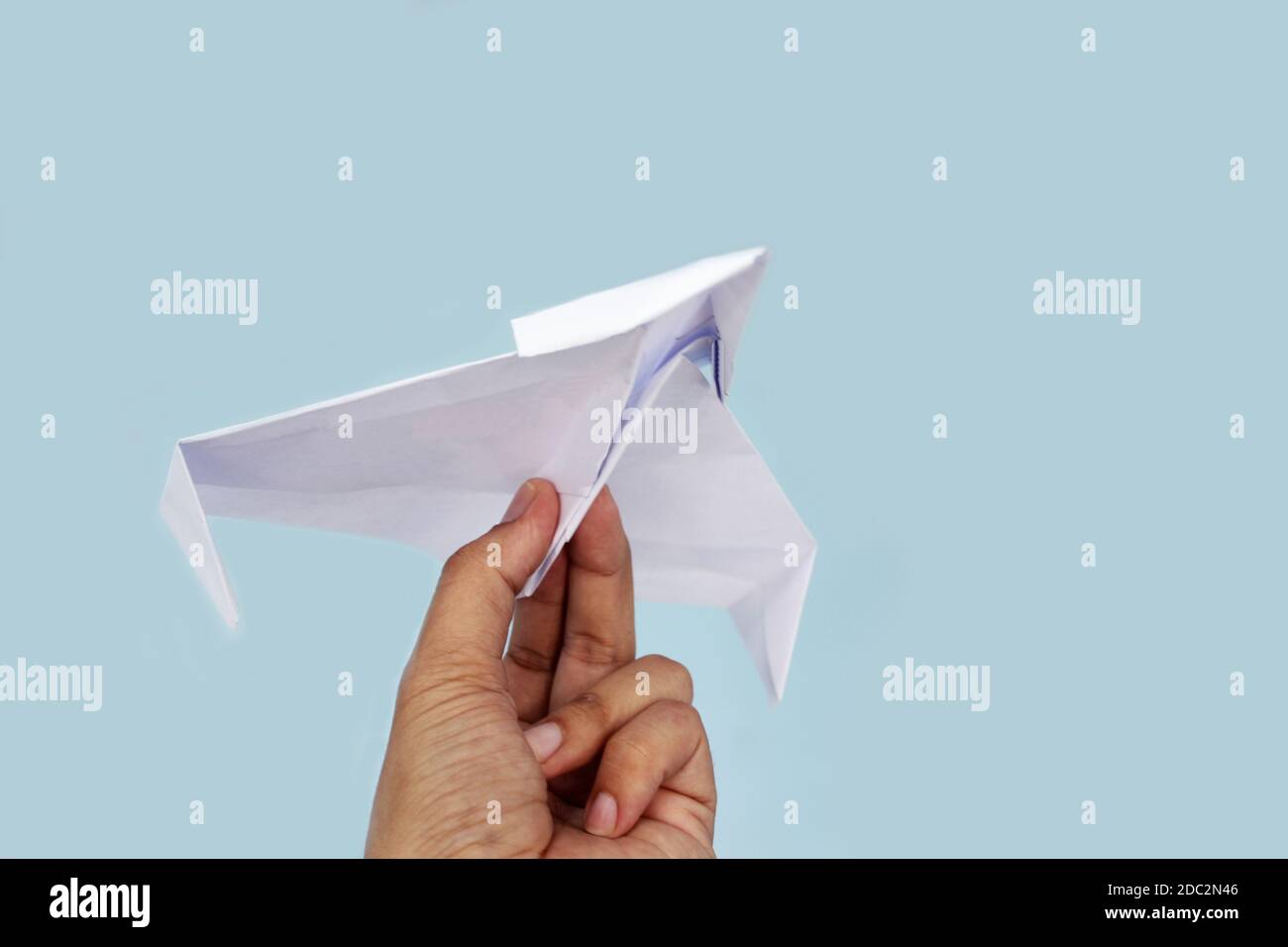 Paper plane on blue background holding in male hand. Stock Photo