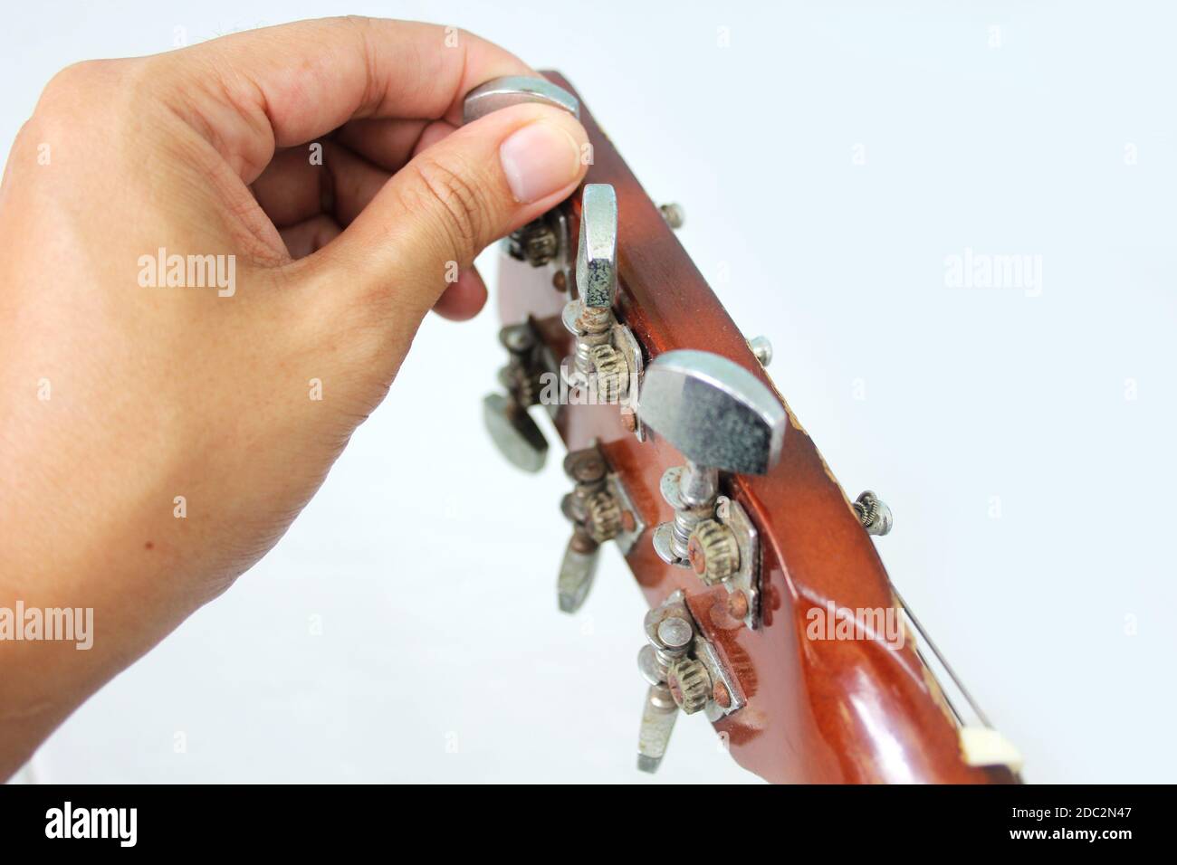 Fingers turning the tuning pegs and gears of the headstock of an