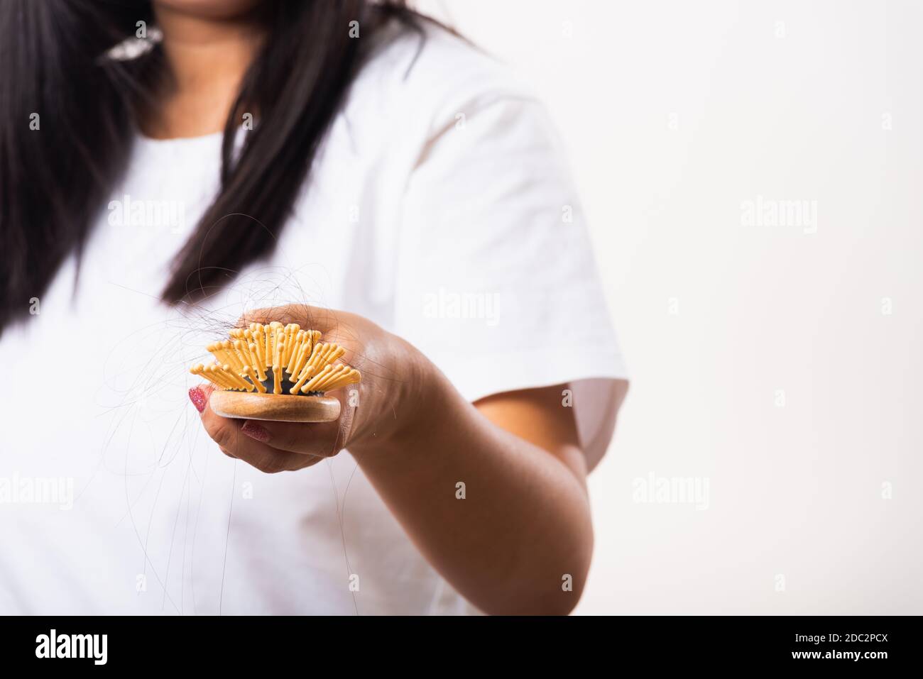 Asian woman unhappy weak hair she shows hairbrush with damaged long loss hair in the comb brush on hand, studio shot isolated on white background, med Stock Photo