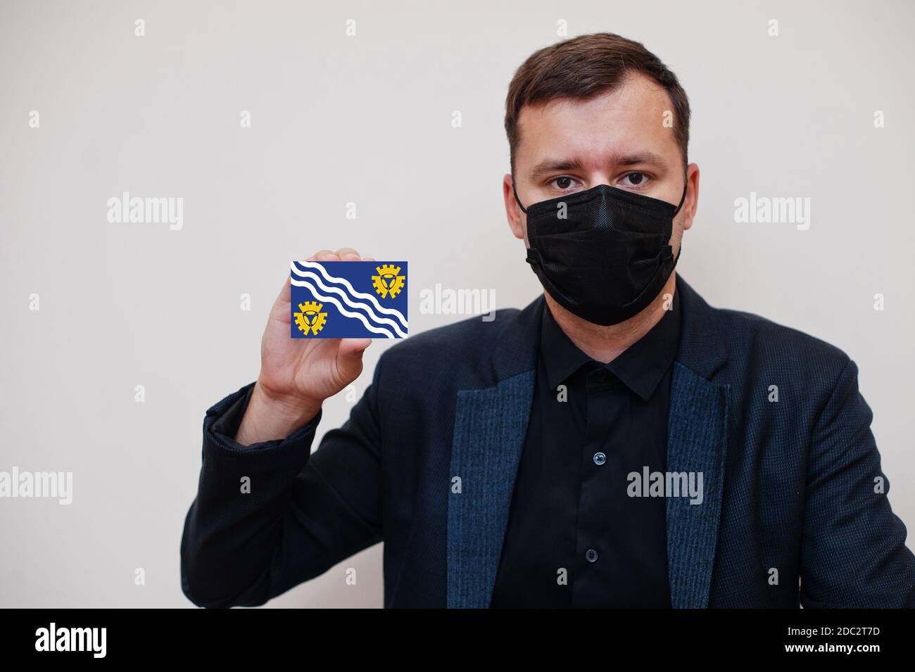 Man wear black formal and protect face mask, hold Merseyside flag card isolated on white background. United Kingdom counties of England coronavirus Co Stock Photo