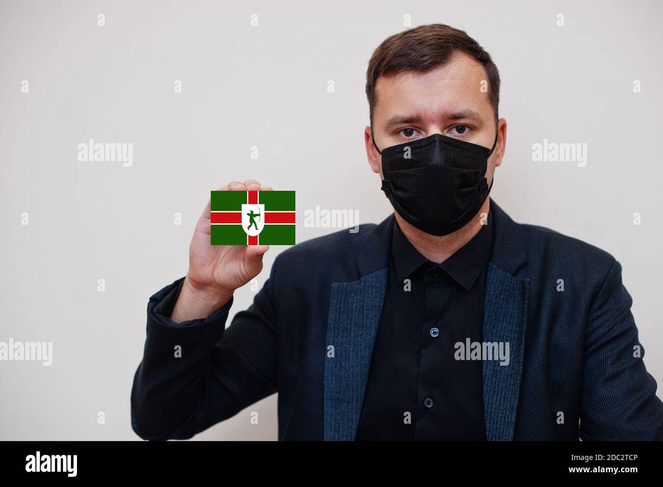 Man wear black formal and protect face mask, hold Nottinghamshire flag card isolated on white background. United Kingdom counties of England coronavir Stock Photo