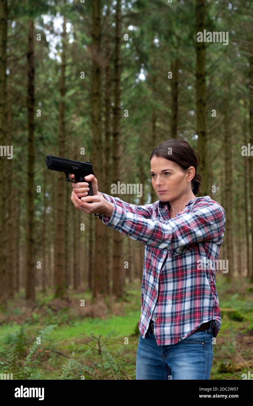 Woman aiming a pistol in the woods, mean expression. Stock Photo