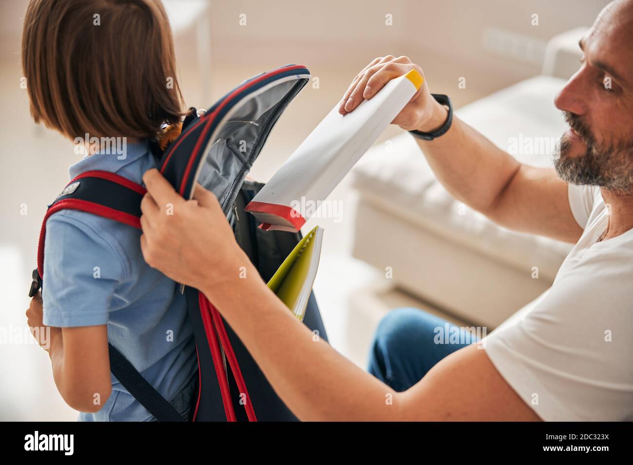 Helpful father packing books into rucksack on his son back Stock Photo