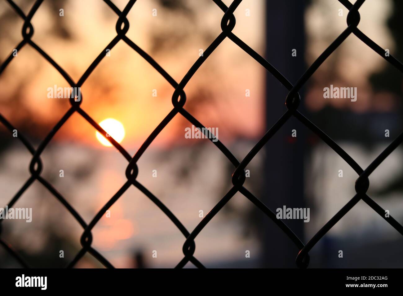View of a sunset through a silhouette fence in urban environment Stock Photo