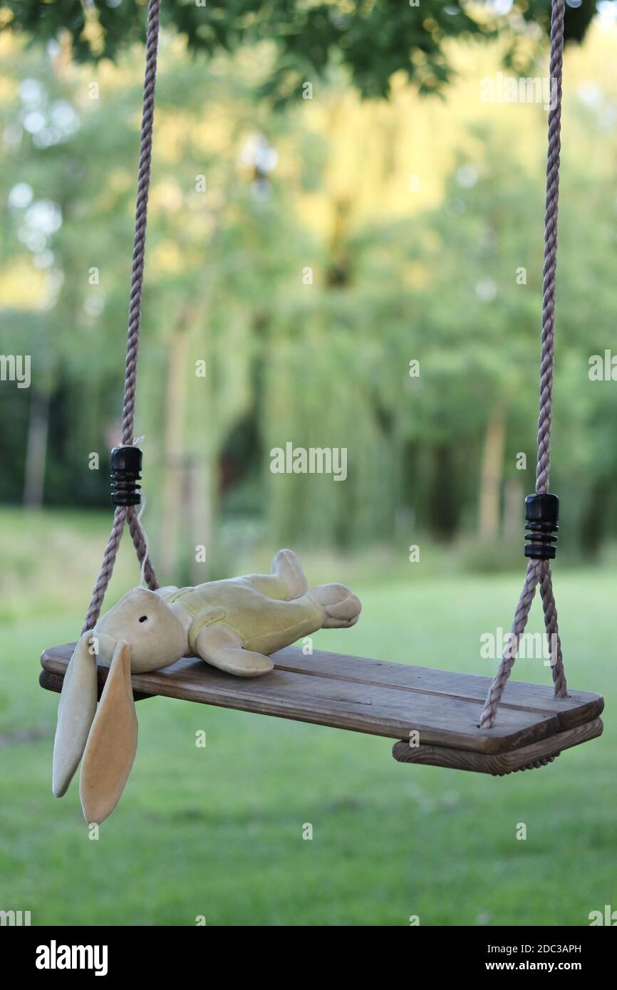 Abandoned stuffed bunny on swing with blurred background, concept for lost or missing child Stock Photo