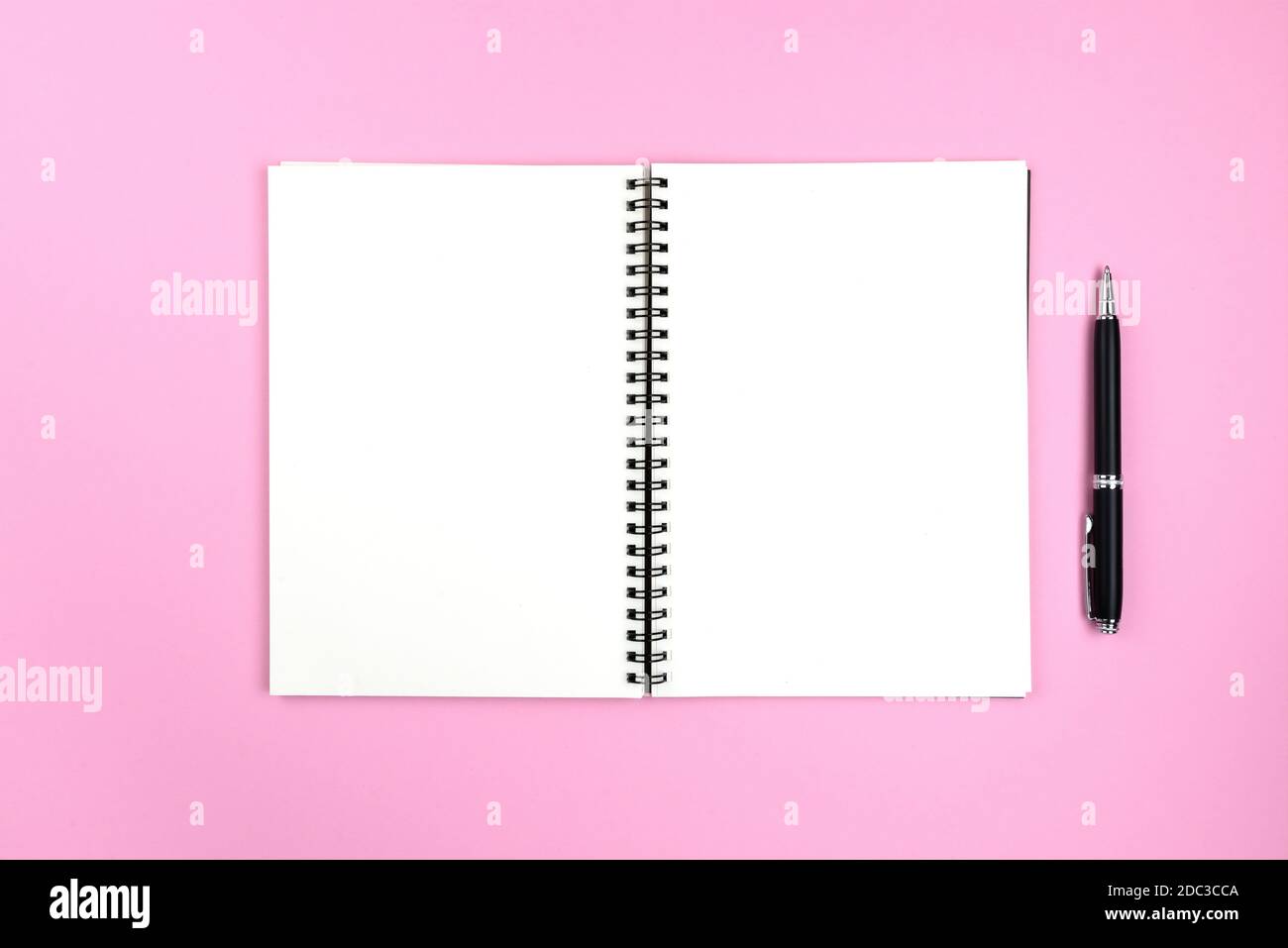 blank pages of open spiral notepad and pencil on pink background Stock Photo