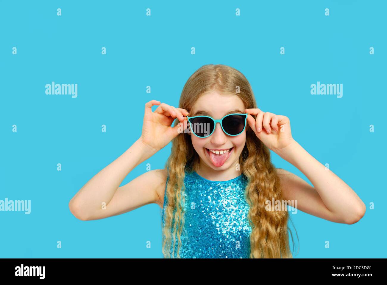 Beautiful mischievous Caucasian little girl in sunglasses shows tongue. The concept of emotions and facial expressions. Stock Photo
