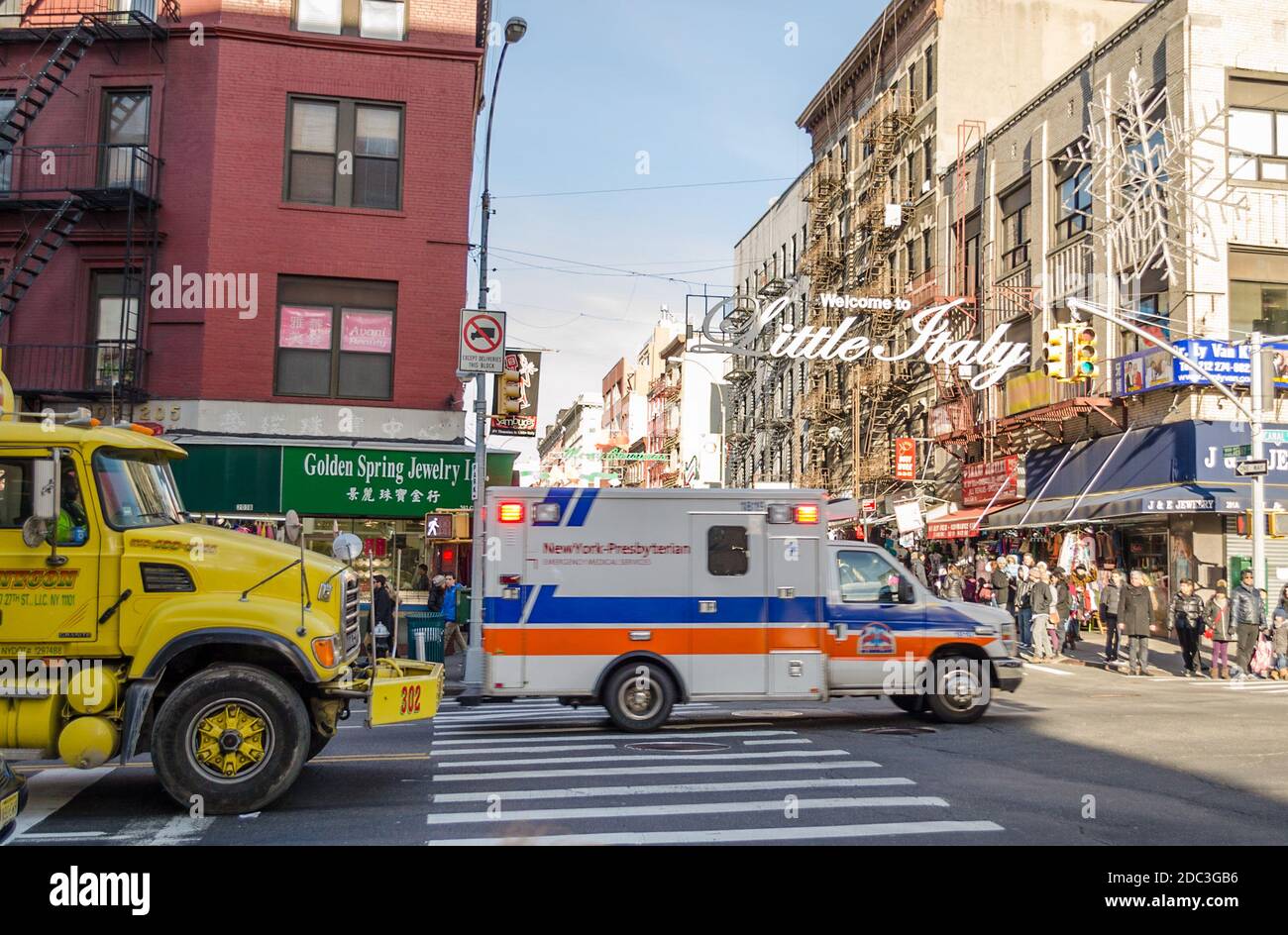 Ordinary Day in Little Italy and Chinatown. Busy Road and Pavement. An Ambulance is passing by the Road and a Yellow Truck Follows Next. Stock Photo