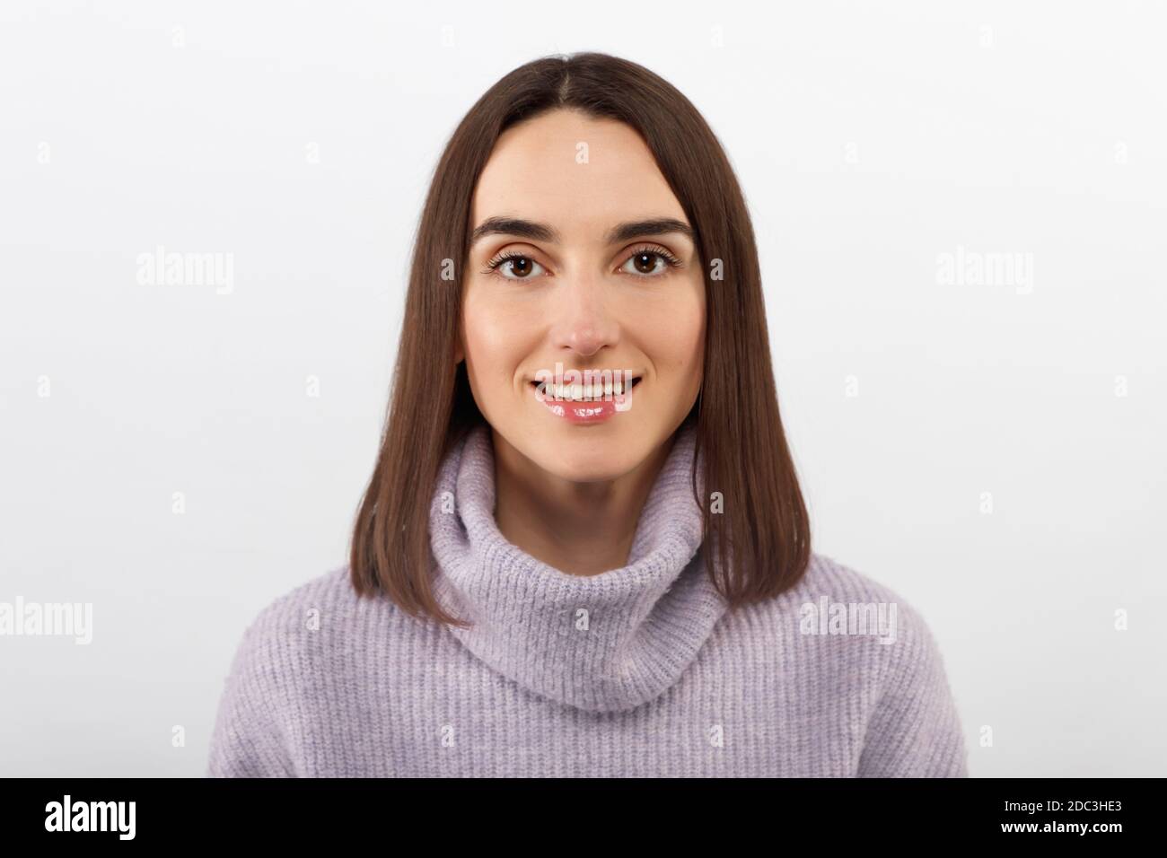 Studio shot of smiling glad woman has appealing appearance, smiles broadly, dressed purple sweater poses against white background expresses positive Stock Photo