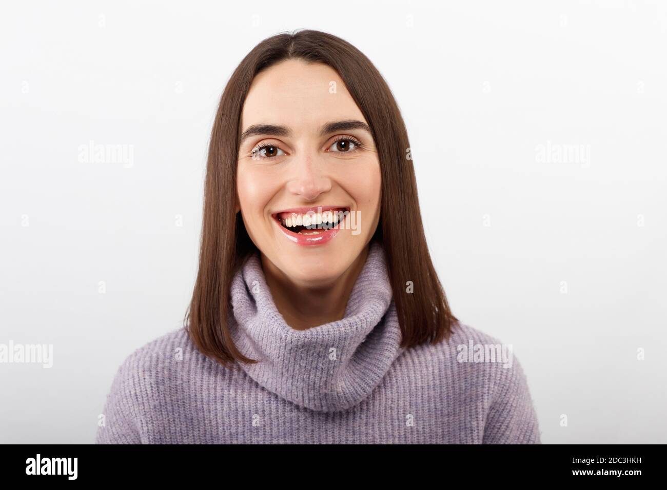 Studio shot of smiling glad woman has appealing appearance, smiles broadly, dressed purple sweater poses against white background expresses positive Stock Photo