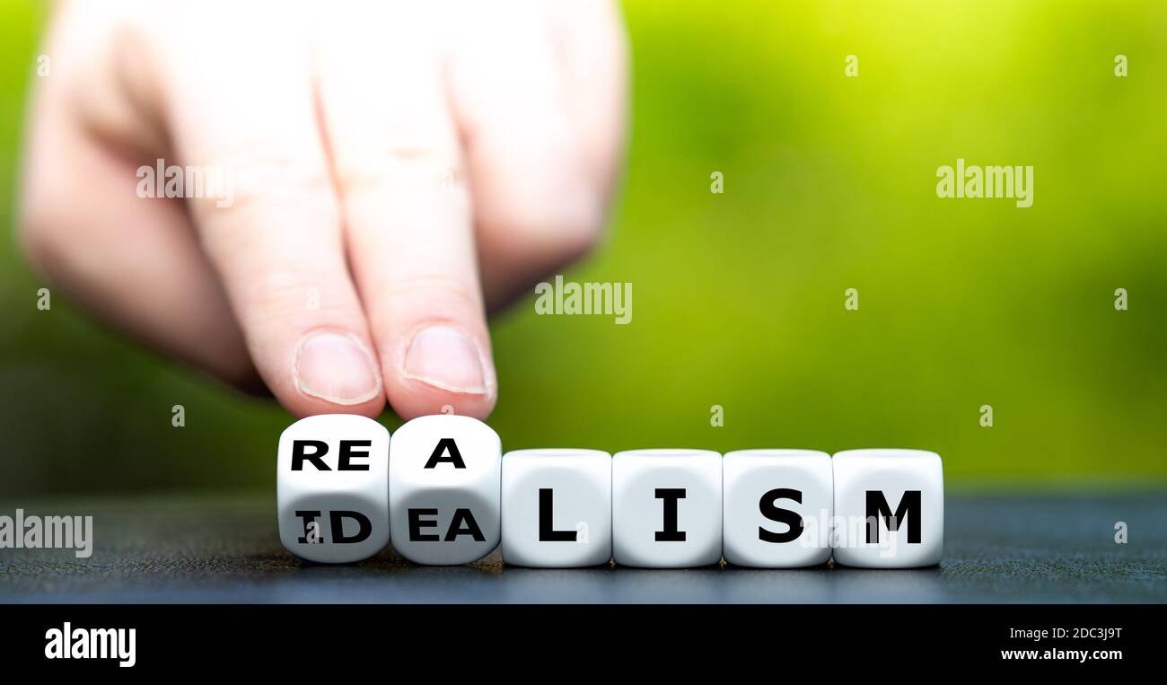 Hand turns dice and changes the word 'idealism' to 'realism'. Stock Photo