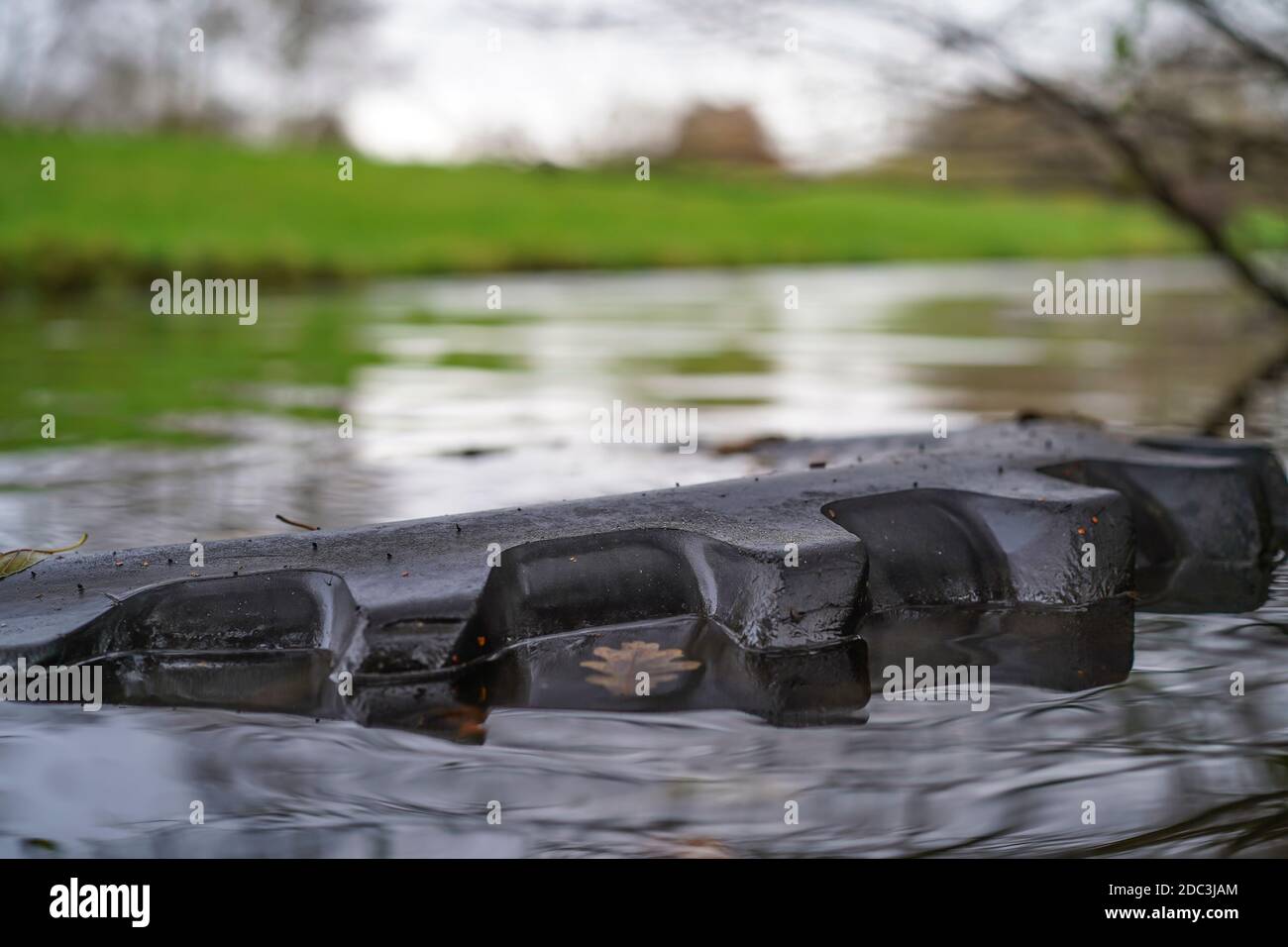 Close up of old JCB vehicle tyre thrown as litter/debris into UK canal seen here partially submerged in water. Eyesore rubbish spoiling countryside. Stock Photo
