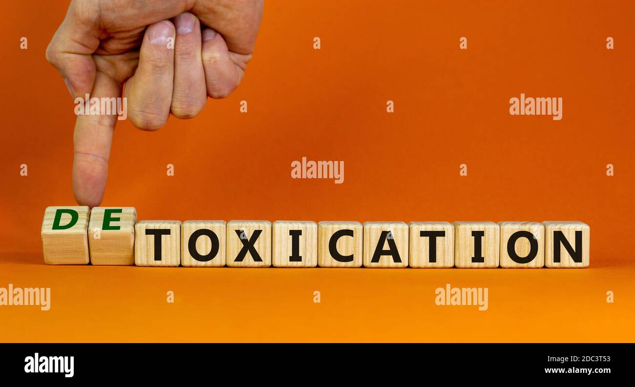 Hand flips cubes and changes the expression 'toxication' to 'detoxication'. Beautiful orange background. Healthy lifestyle concept. Copy space. Stock Photo