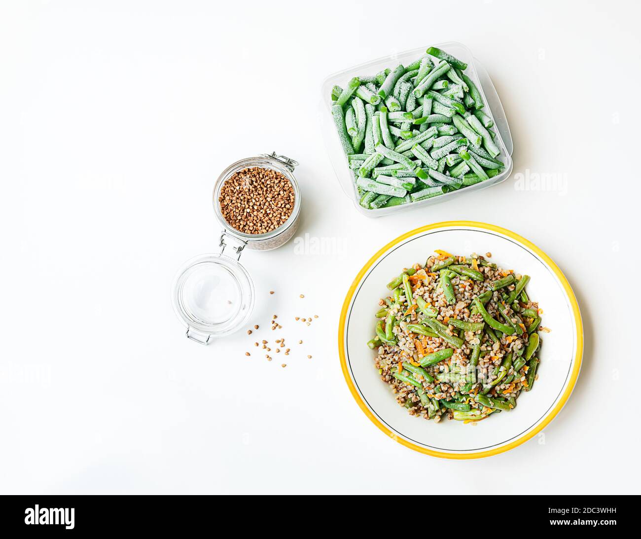 Buckwheat porridge with green beans and ingredients for its preparation - frozen green beens and buckwheat in a glass jar on the white table, healthy Stock Photo