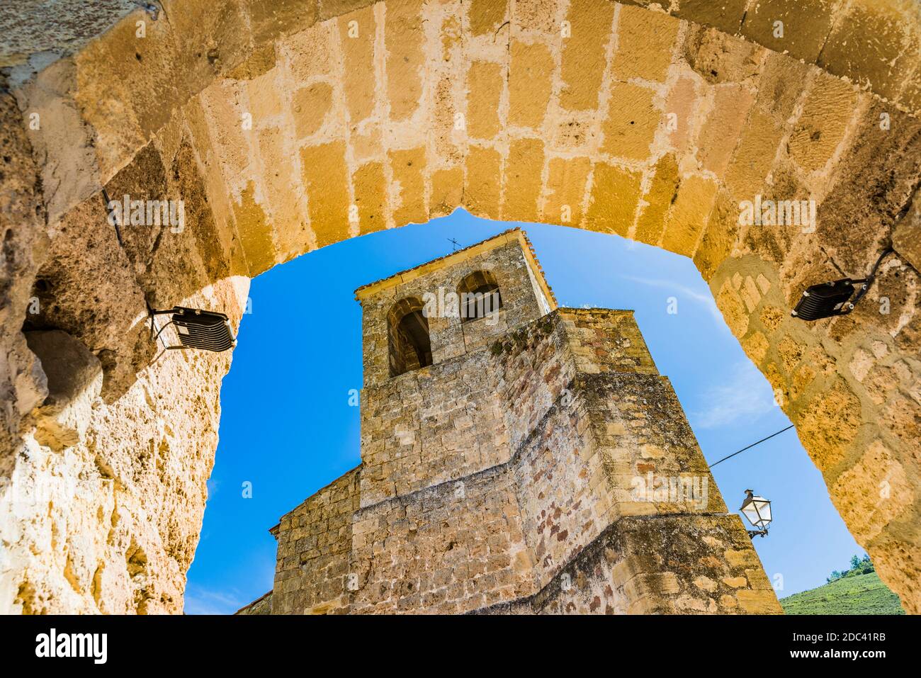 The bell tower of the church of Santa Maria seen through the medieval arch at the entrance of the town.Tubilla del Agua, Valle del Rudrón, region of P Stock Photo