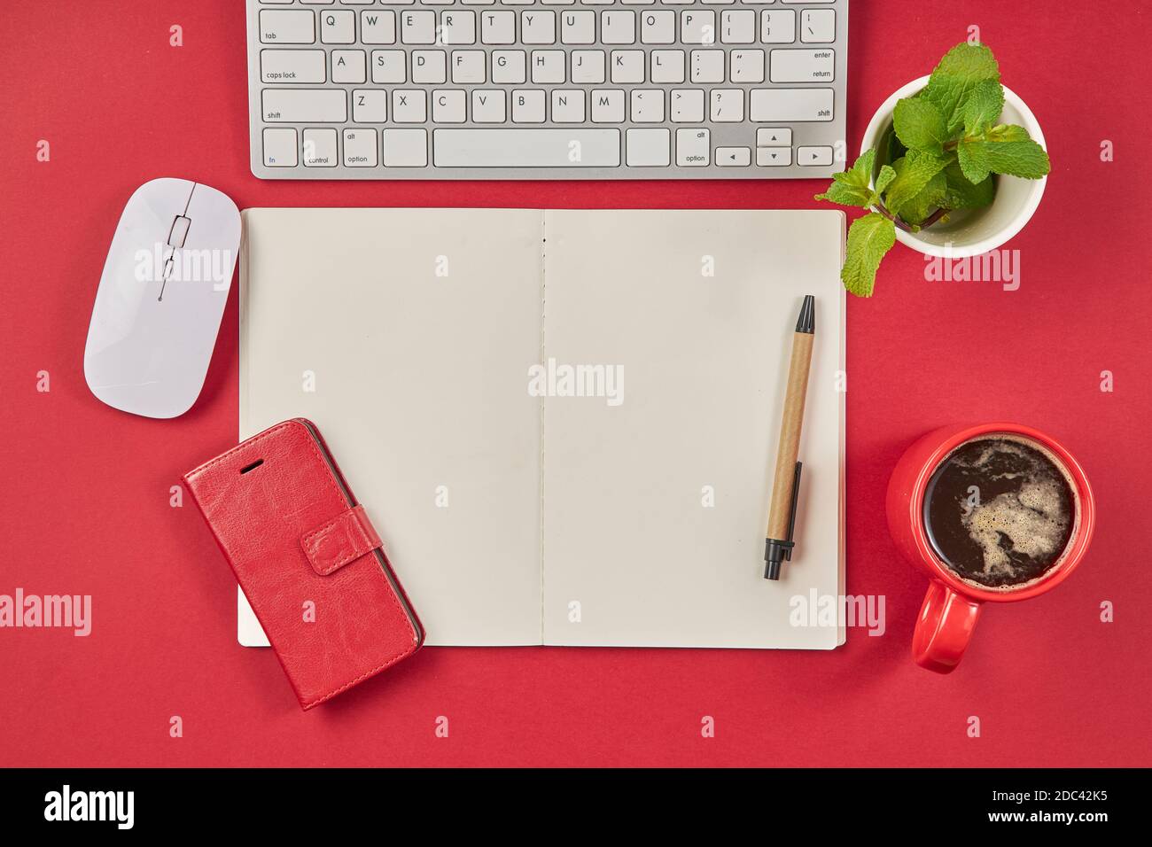 Red office desk table with blank notebook, keyboard and coffee cup. Top view with copy space. Stock Photo