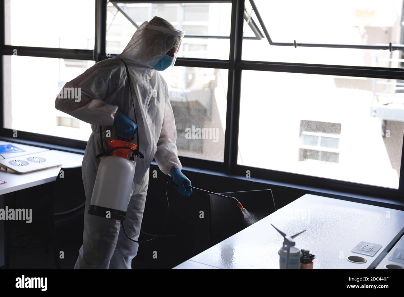Health worker wearing protective clothes cleaning office using disinfectant Stock Photo