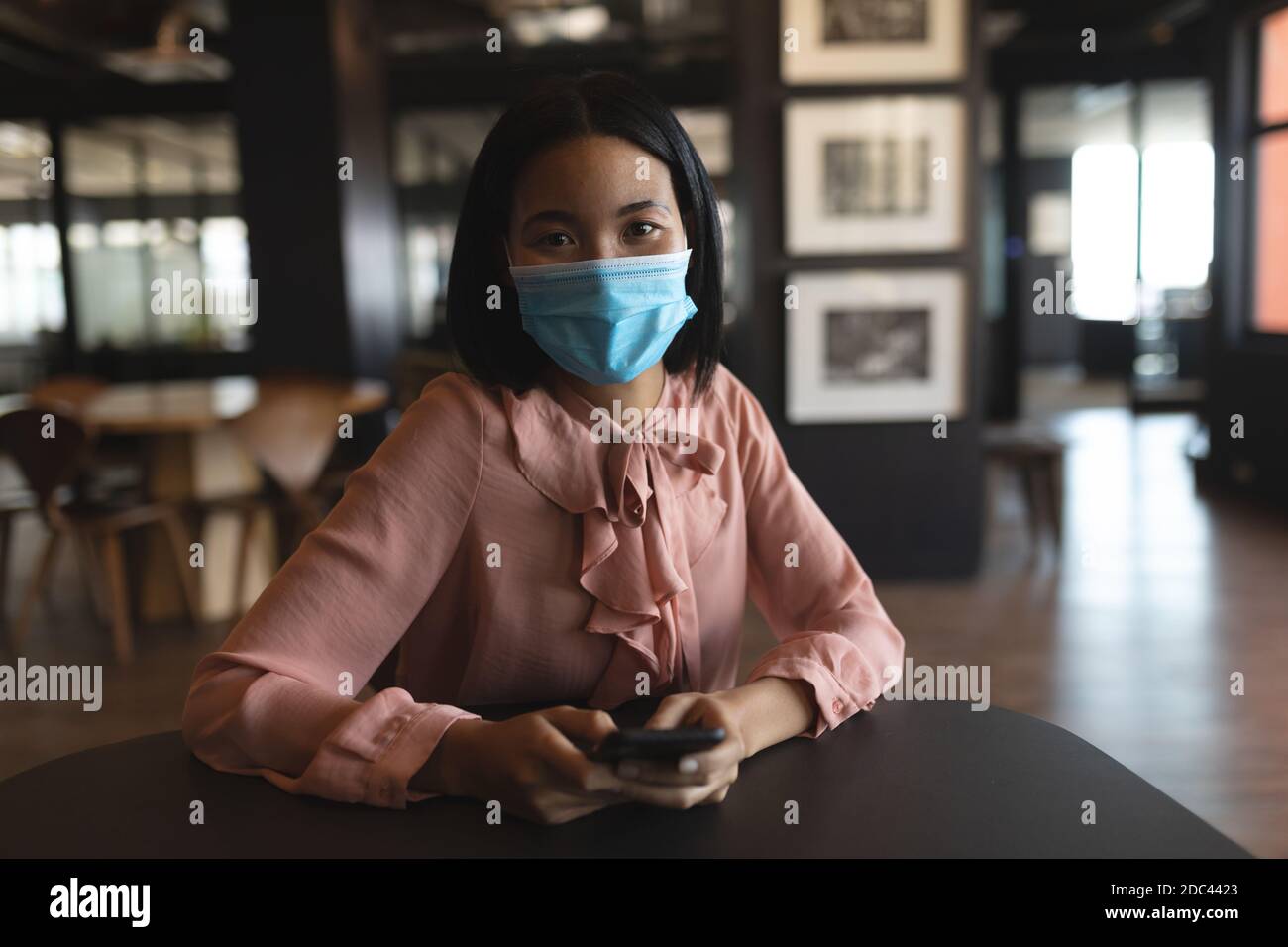 Portrait of asian woman wearing face mask holding smartphone at modern office Stock Photo