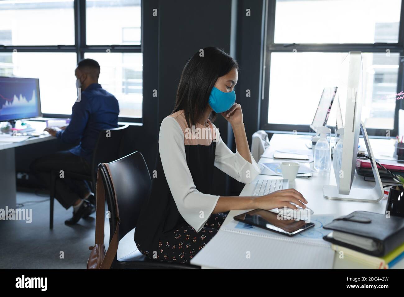 Asian woman wearing face mask using computer while sitting on her desk ...