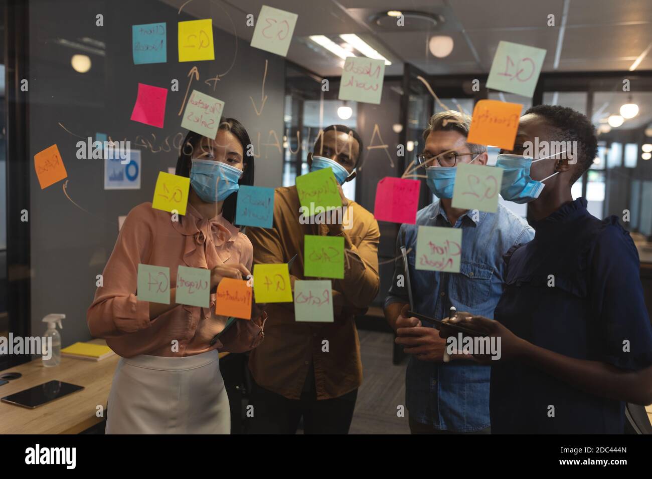 Diverse office colleagues wearing face masks brainstorming in office Stock Photo