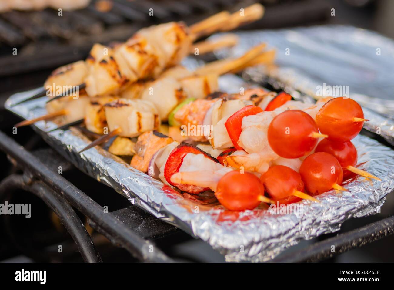 Cooked scallop and shrimp, prawn skewers, cherry tomato on foil - street food Stock Photo