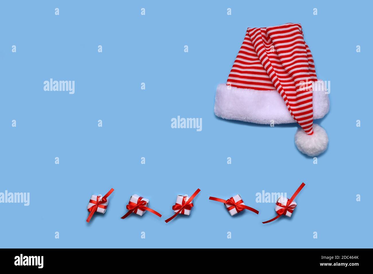 Santa's striped hat, laid out on a blue background. Below are white papered gifts and bandaged red ribbon with a bow. Stock Photo