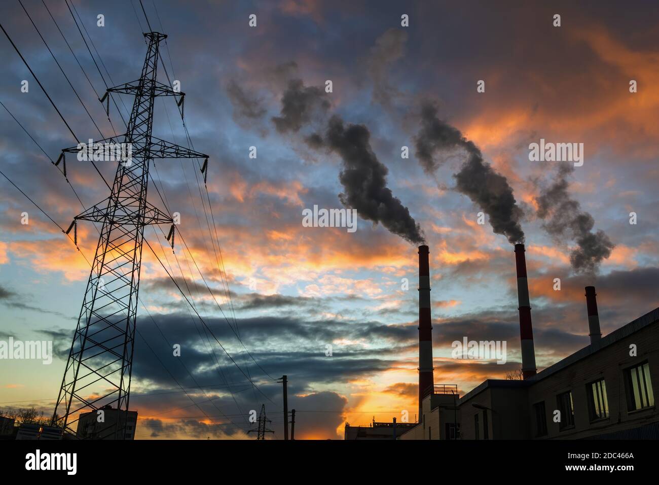 Silhouette of steel lattice tower, three chimneys smoke on dramatic sunset sky background. Transmission tower and industry pipes. Industrial cityscape Stock Photo