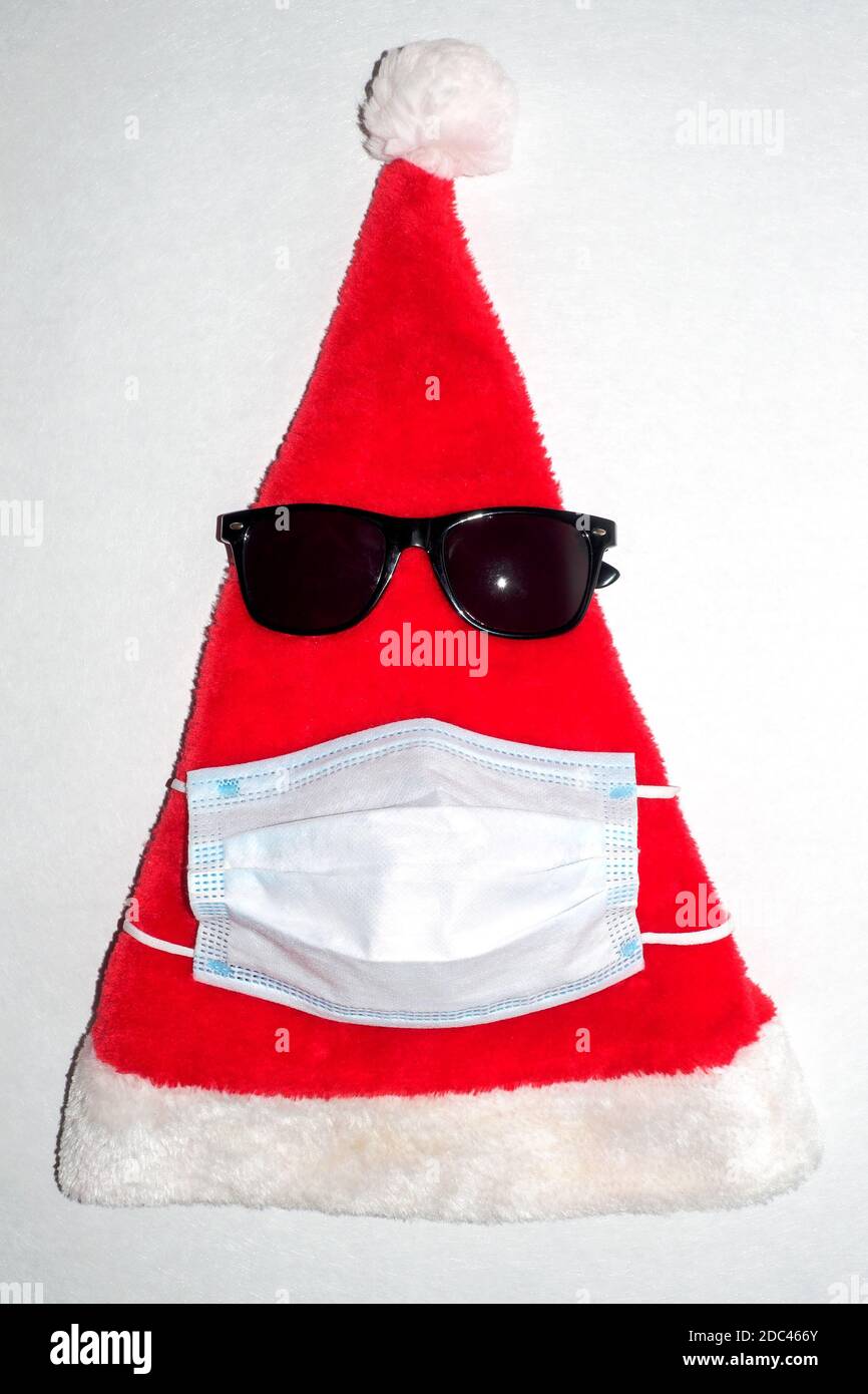 Red and White Plush Christmas Santa Hat with black glasses and medical mask. Vertical top view Stock Photo